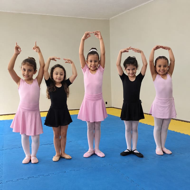 Cinco meninas de collant e saia de ballet, em fila sobre o tatame azul, com os braços erguidos acima da cabeça