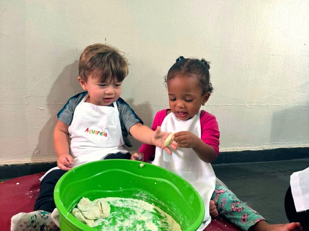 Duas crianças pequenas de babador Aquarela brincam com massinha em uma bacia verde