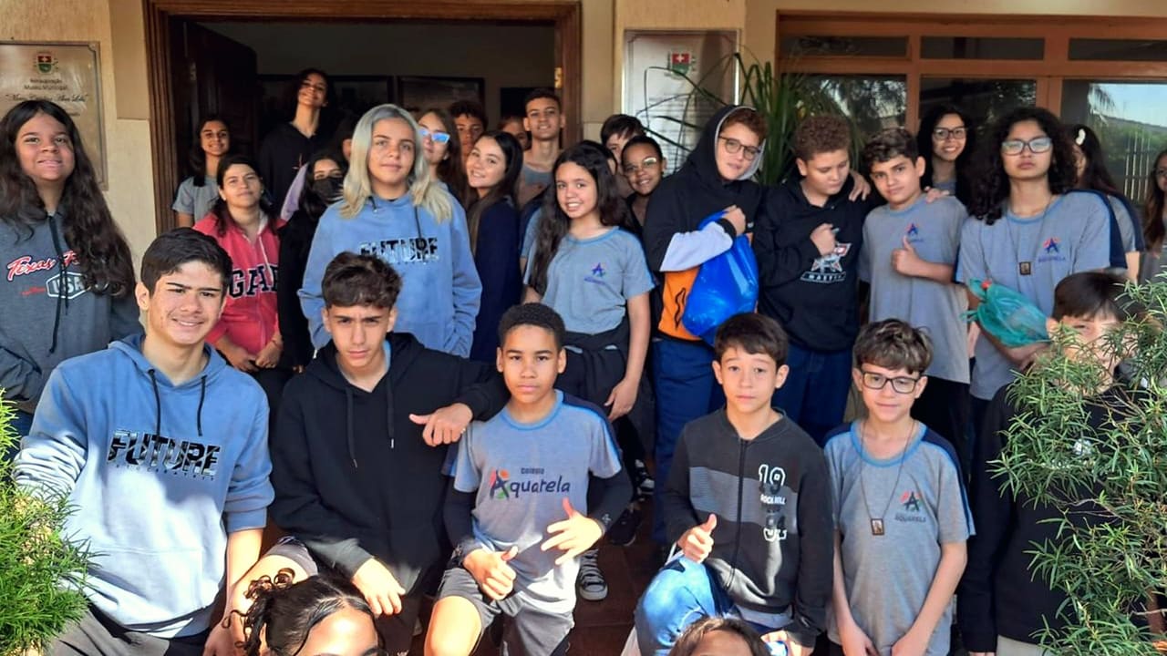 Grande grupo de alunos de uniforme reunido na entrada da escola, sorrindo para a foto